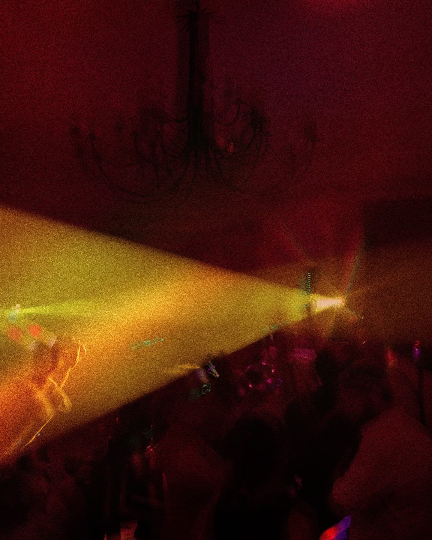 A wide light beam cutting through a dark red room over the crowd