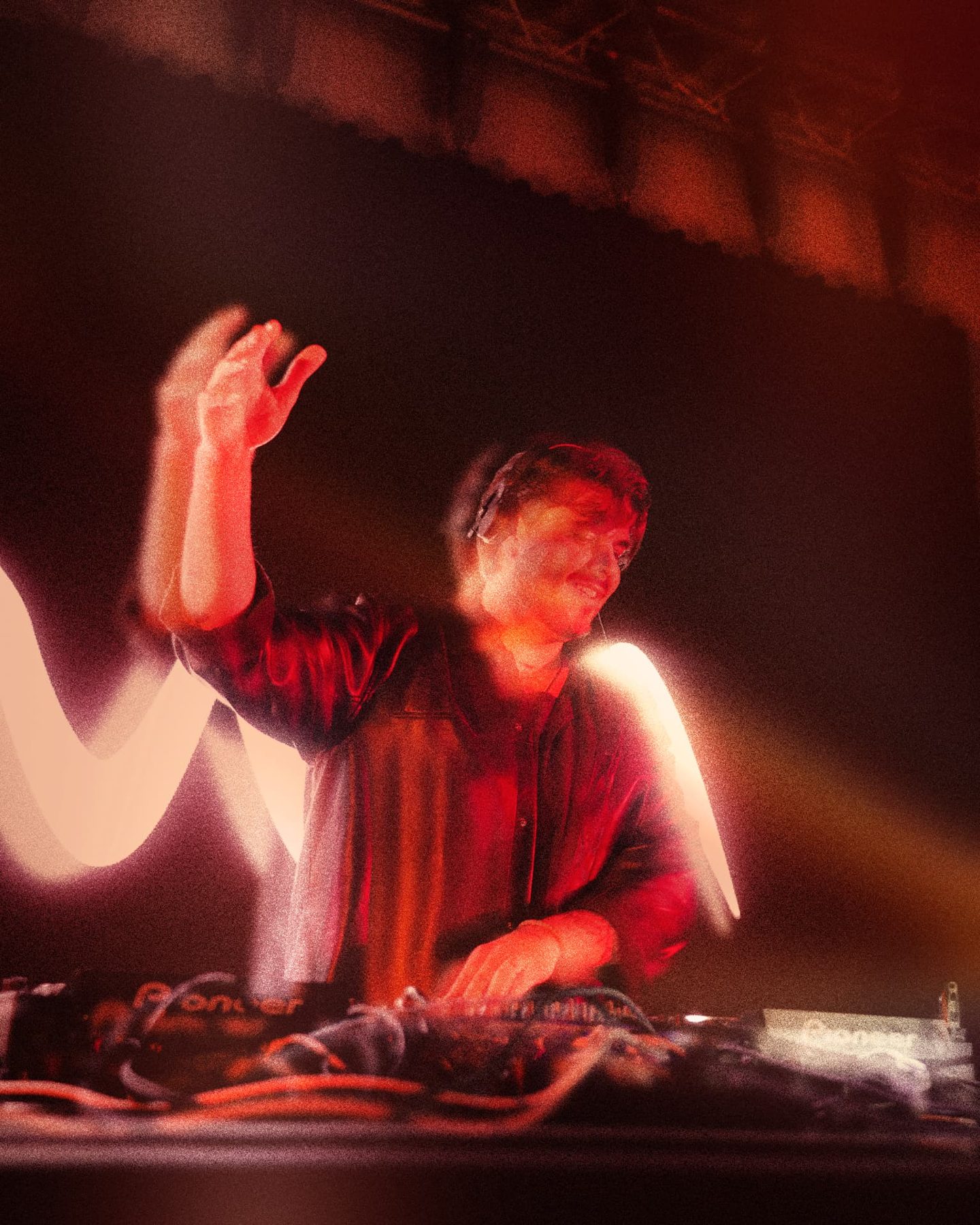 DJ raising a hand over the decks in red light